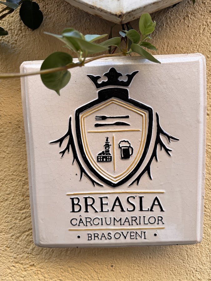 Însemn ceramic al Breslei Cârciumarilor Brașoveni, cu tacâmuri, Casa Sfatului și o halbă, pe un perete galben