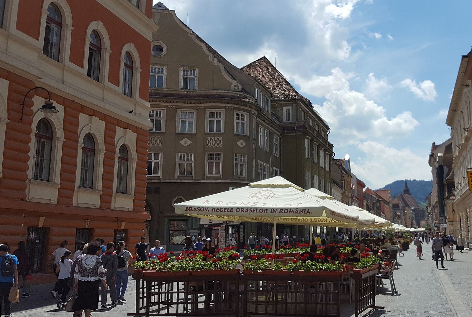 Strada Republicii, pietonală, cu terase și flori, iar în fundal Muntele Tâmpa