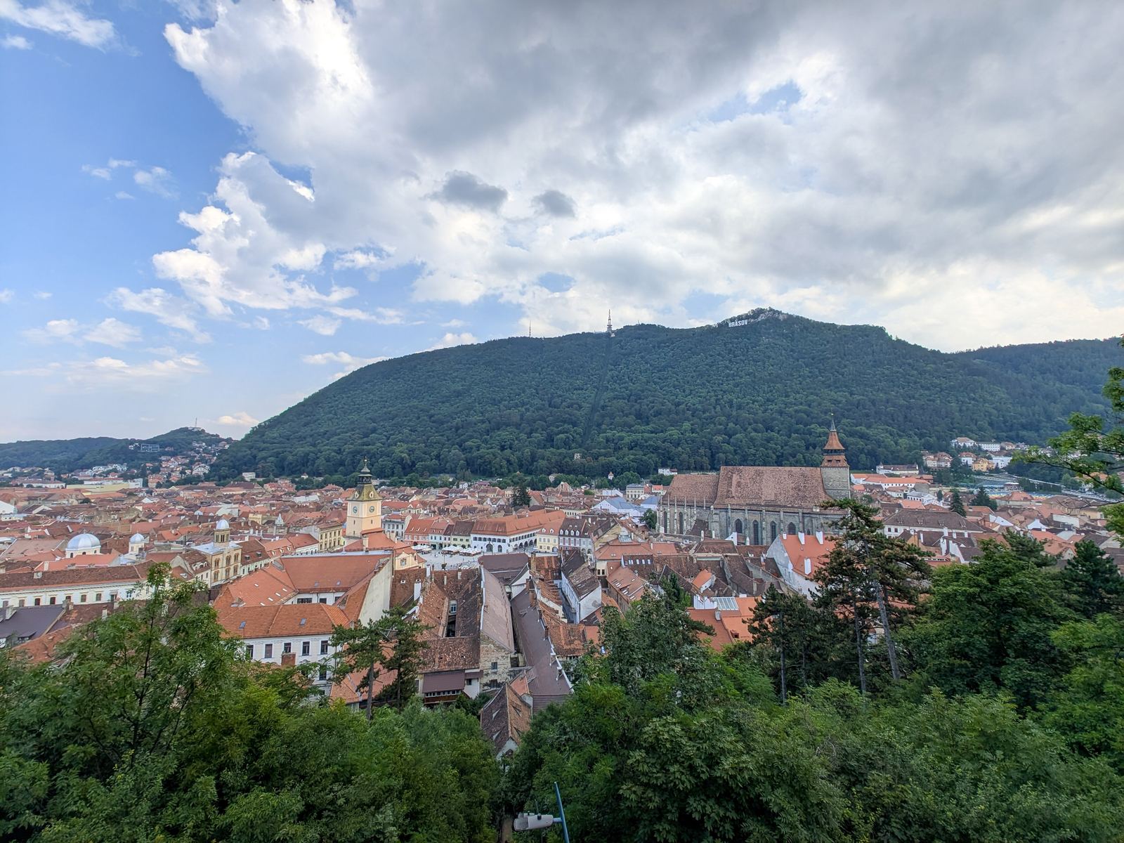 Acoperișurile roșii ale centrului istoric, Biserica Neagră și Muntele Tâmpa, sub un cer senin cu nori
